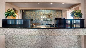 A reception desk with a marble countertop, two potted plants, and a wall with the text "Econo Lodge BY Choice Hotels".