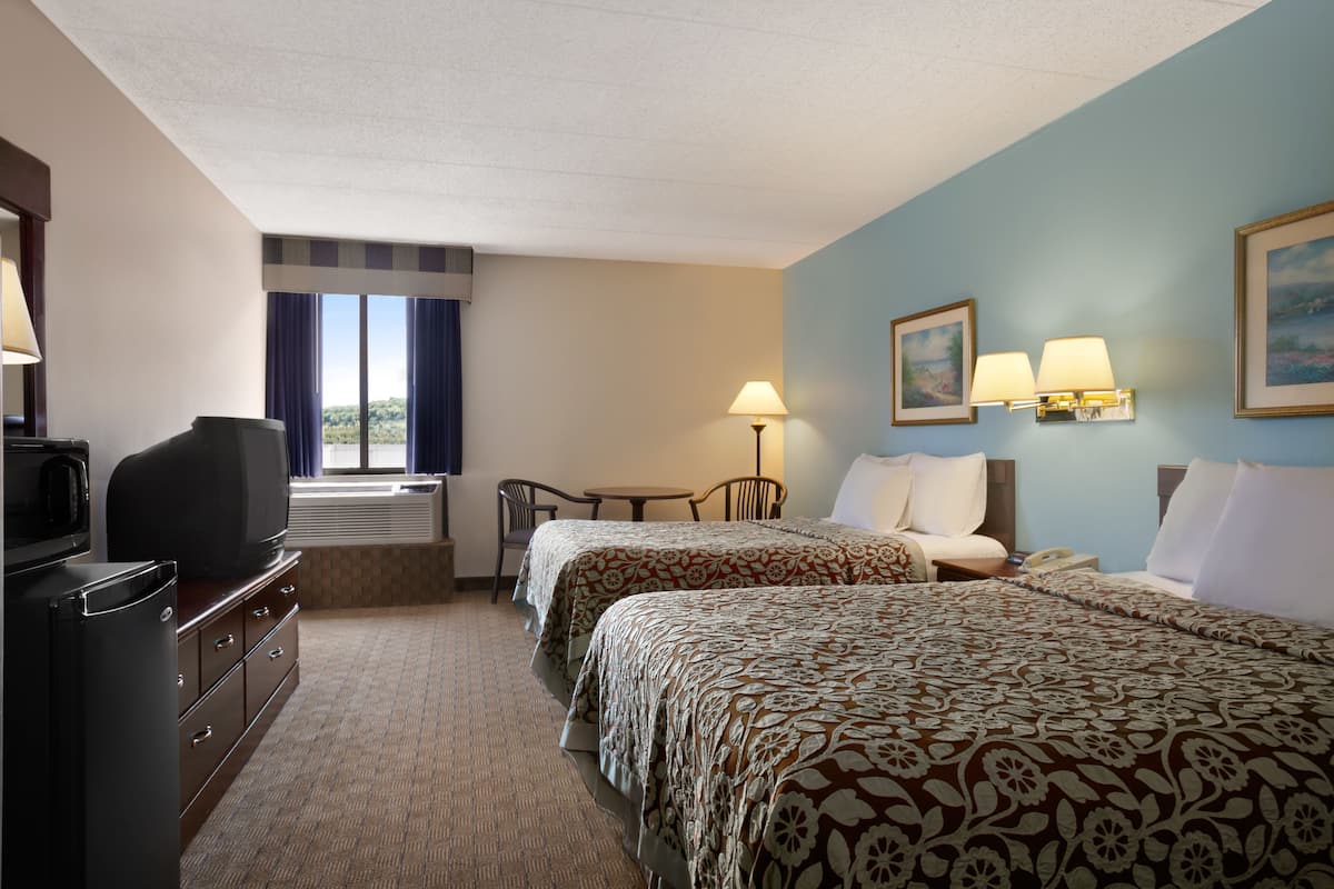A hotel room with two beds, a desk, a chair, a television, and a window with curtains.