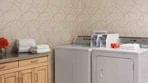 A laundry area with a washing machine and dryer, a wooden cabinet, and a vase with flowers. - Days Inn by Wyndham Reading Wyomissing (Wyomissing)