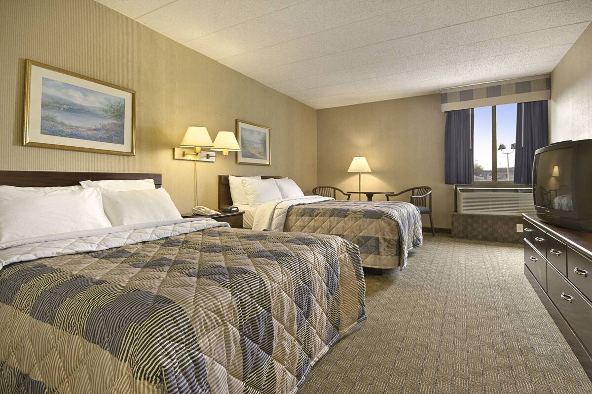 A hotel room with two beds, a TV, a desk, and a window with curtains.