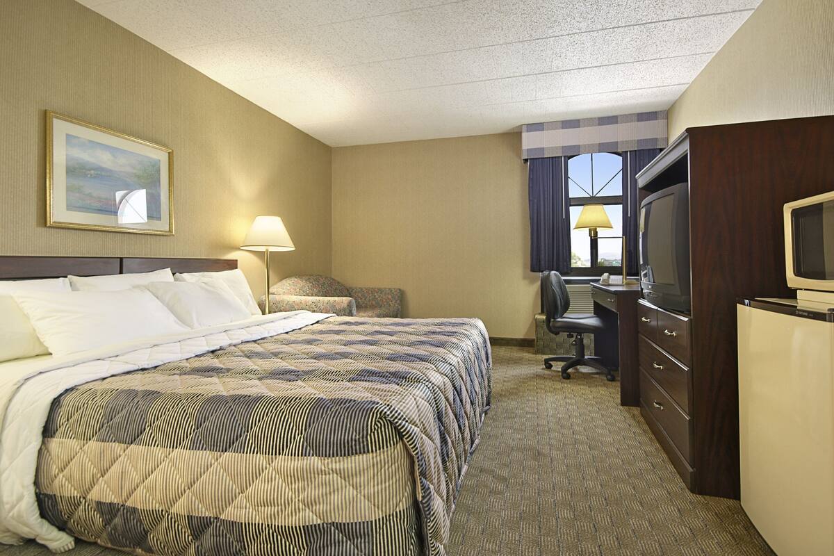 A hotel room with a large bed, a desk with a computer, a television, and a window with curtains.