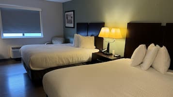 Habitación de hotel con dos camas, una mesita de noche con lámpara, una silla y una ventana con persianas.