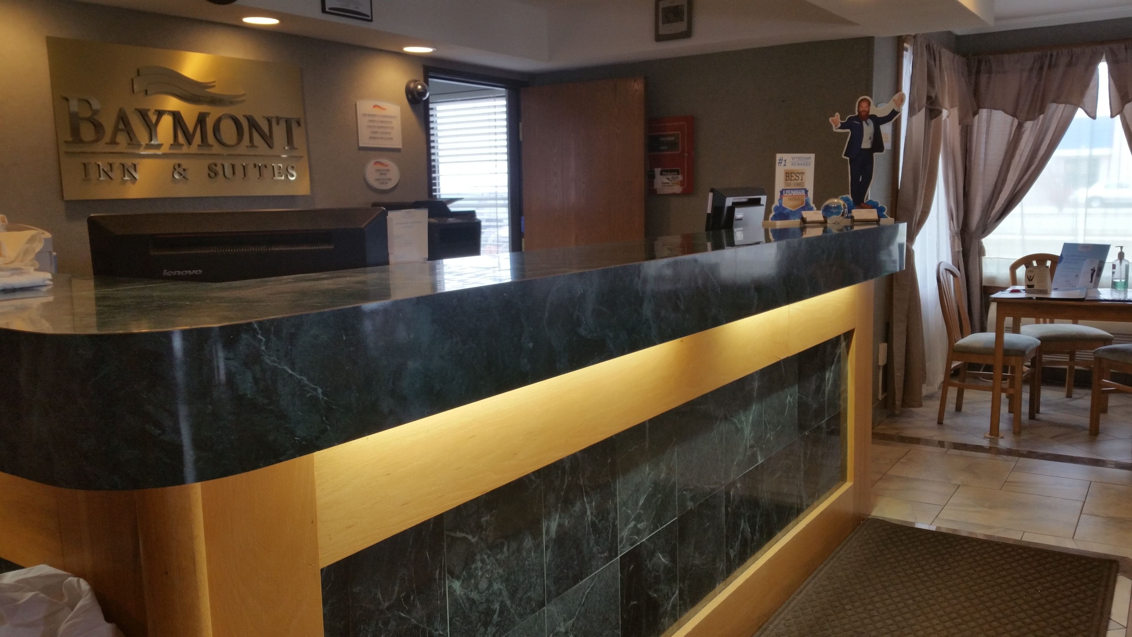 Una reception con un piano in marmo nero e dettagli dorati, un computer Lenovo e un cartello con la scritta Baymont Inn & Suites.