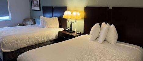 A hotel room with two beds, a nightstand with a lamp, a framed picture on the wall, and a window with blinds.