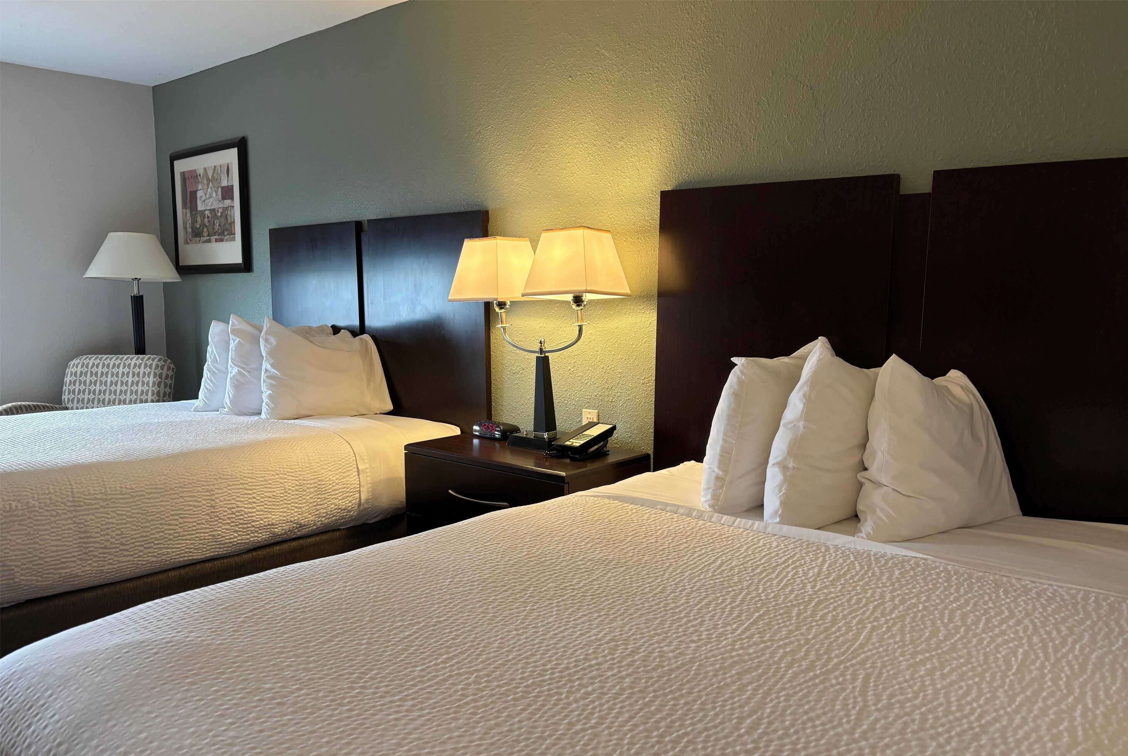 A hotel room with two beds, a nightstand with a lamp, and a framed picture on the wall.