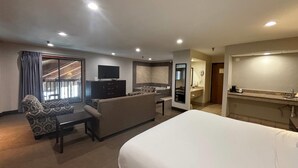 A hotel room with a large bed, a sofa, a desk, a television, and a kitchen area. - Baymont by Wyndham Tuscola (Tuscola)