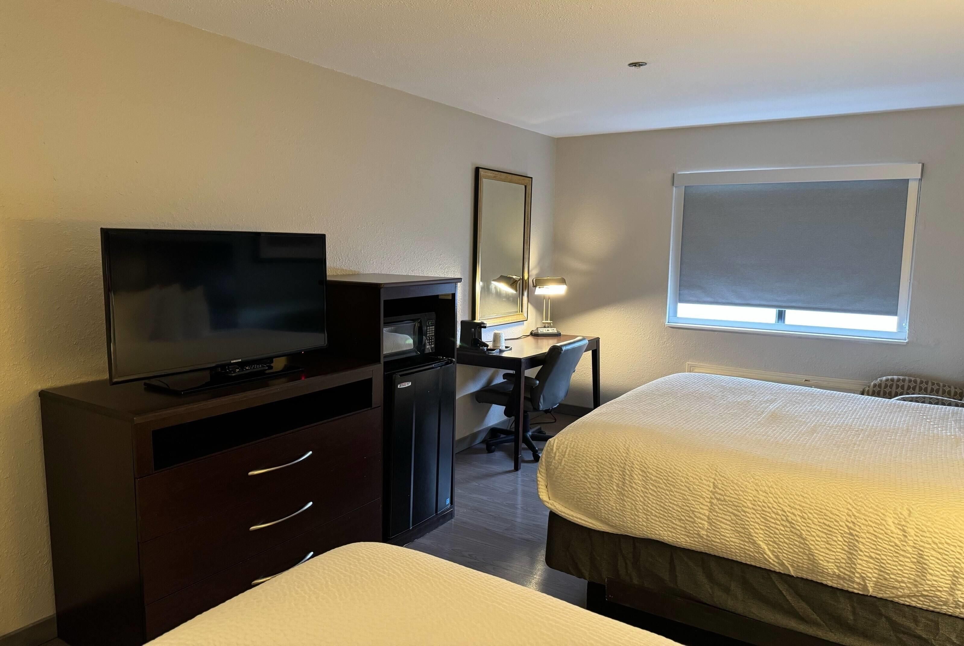 A hotel room with a bed, a desk with a chair, a television, a microwave, and a large window.