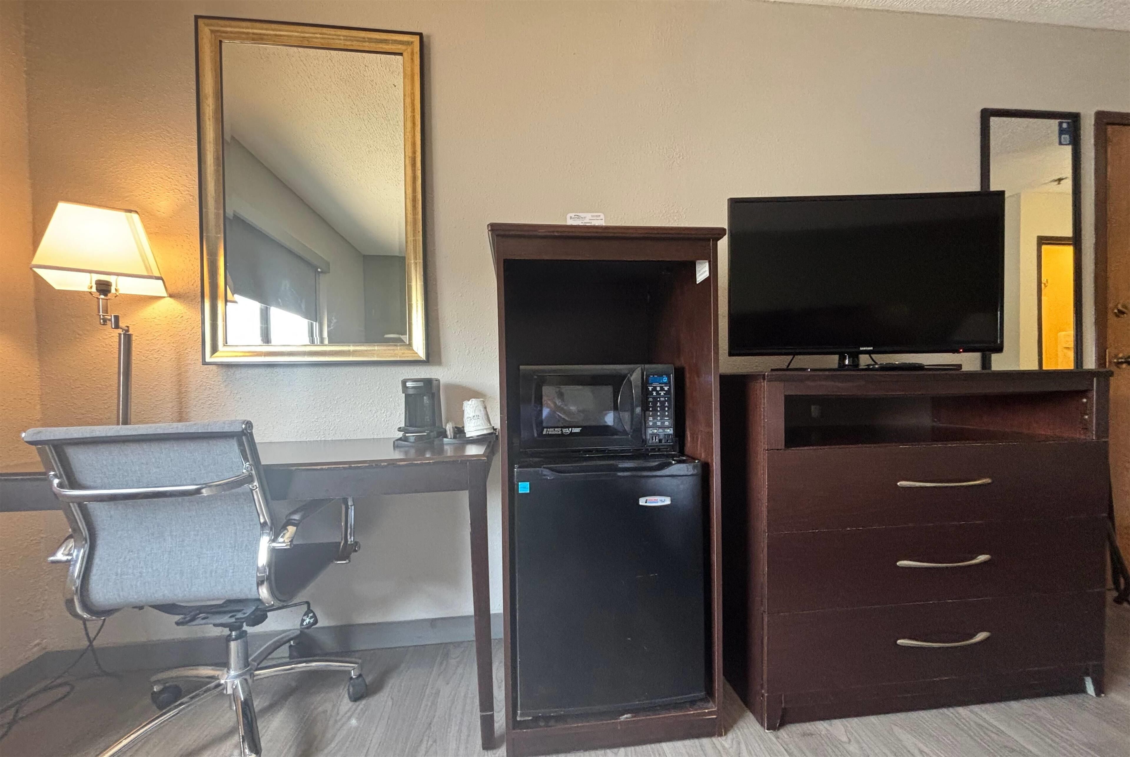 Una habitación de hotel con escritorio, silla de oficina, microondas, televisor y cómoda.