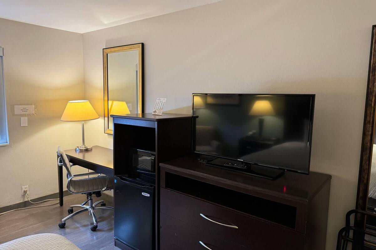 A hotel room with a desk, chair, television, and a mirror.