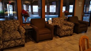 A lobby with patterned armchairs, a small table with a vase of flowers, and large windows with a view of the outside. - Baymont by Wyndham Tuscola (Tuscola)