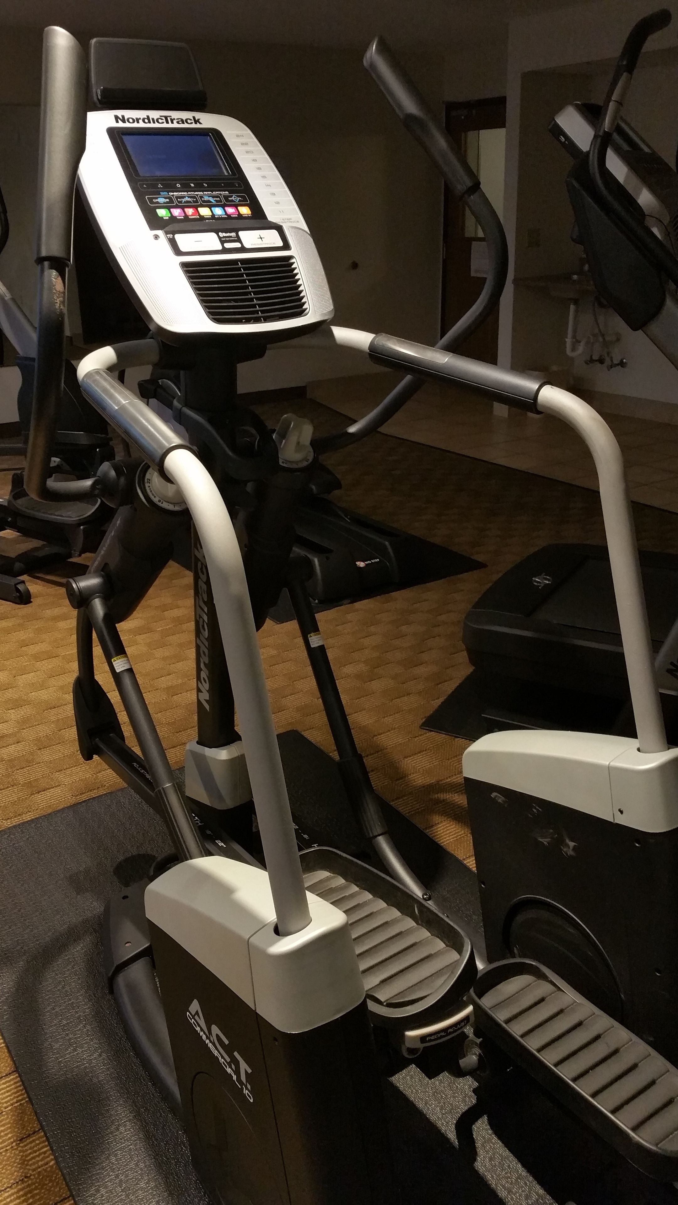 A NordicTrack elliptical machine with a digital display and control panel, positioned on a black mat in a gym setting.