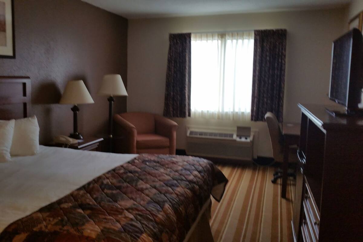 A hotel room with a large bed, a desk with a lamp, a chair, a television, and a window with curtains.