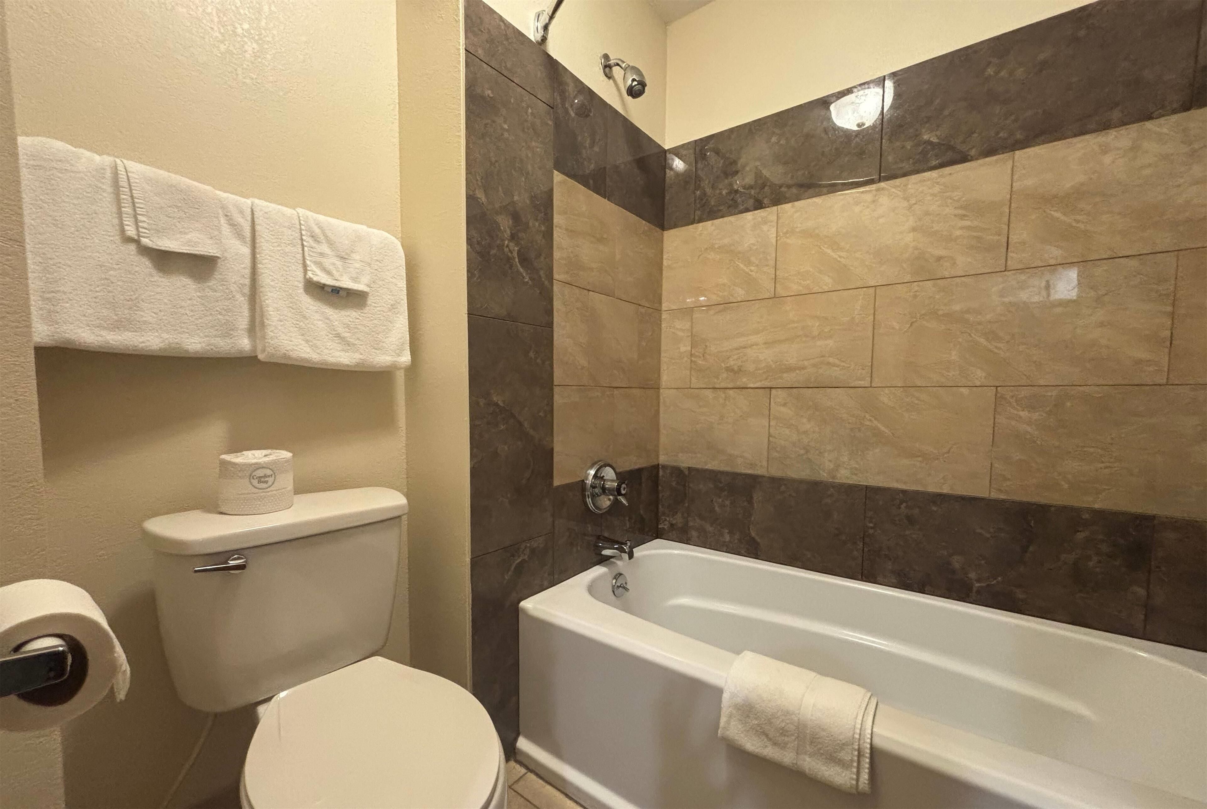 Une salle de bain comprenant des toilettes, un rouleau de papier toilette, un porte-serviettes avec deux serviettes et une baignoire.