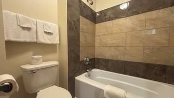 Une salle de bain comprenant des toilettes, un rouleau de papier toilette, un porte-serviettes avec deux serviettes et une baignoire.