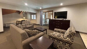 A living room with a sofa, armchairs, a coffee table, a TV, and a sliding glass door leading to a balcony. - Baymont by Wyndham Tuscola (Tuscola)