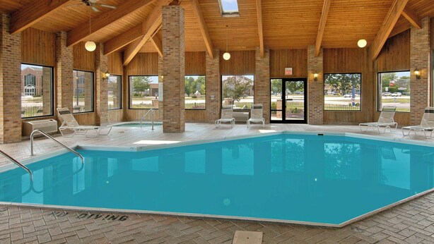 A large indoor swimming pool with clear views of the outside, surrounded by lounge chairs and a wooden ceiling structure. - Baymont by Wyndham Tuscola (Tuscola)
