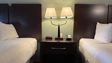 A hotel room with two beds, a nightstand with a lamp, a clock, and a phone.