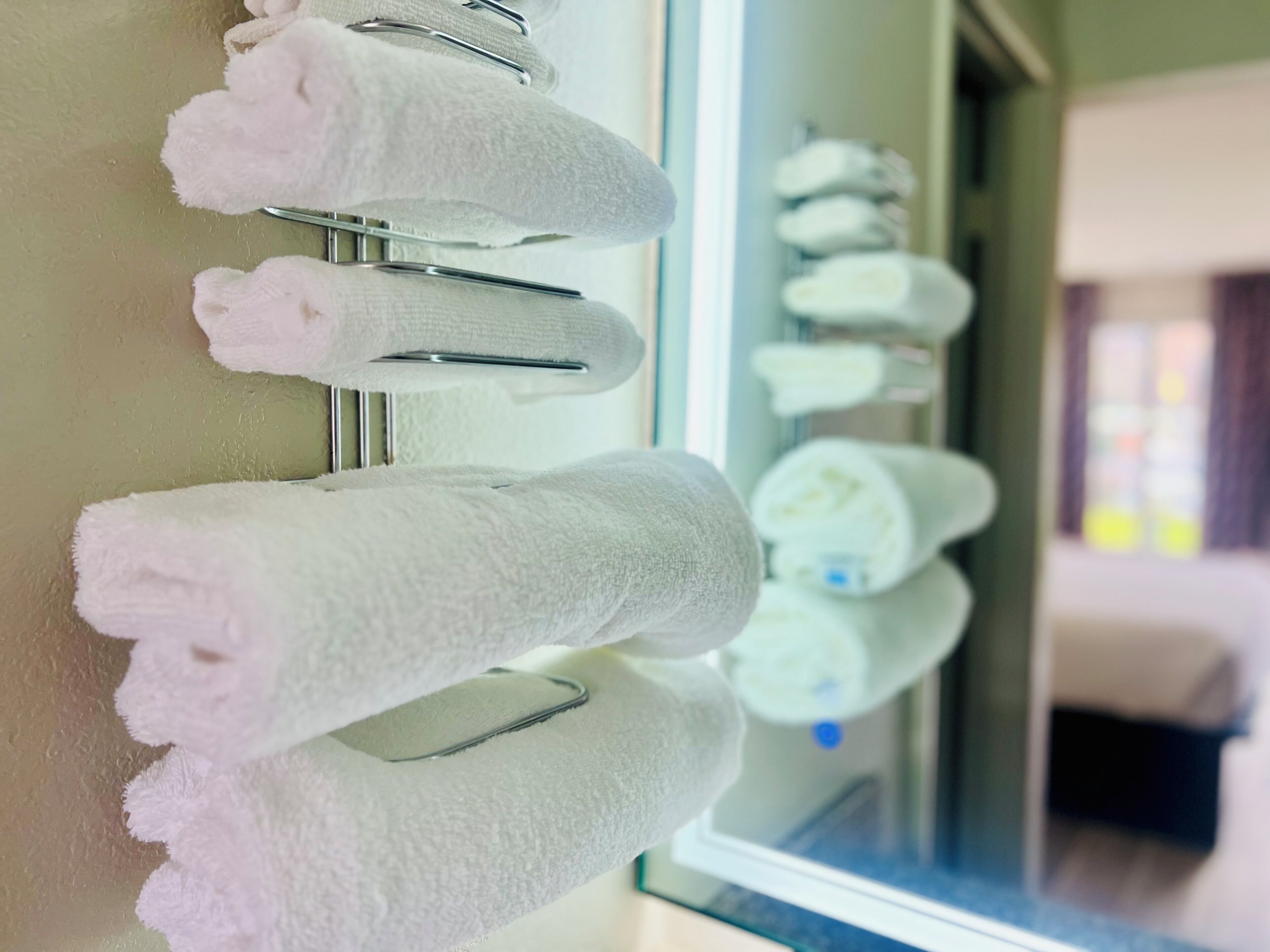 A row of neatly folded white towels hanging on a metal rack in a hotel room.