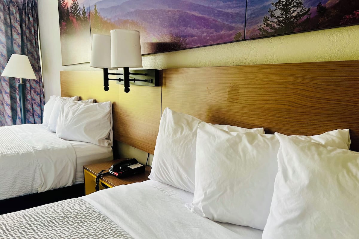 Ein Hotelzimmer mit zwei Betten, einem Holzkopfende, einem Nachttisch mit Telefon und einer Wandlampe.