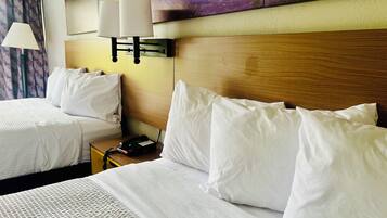 A hotel room with two beds, a wooden headboard, a nightstand with a phone, and a wall-mounted lamp.