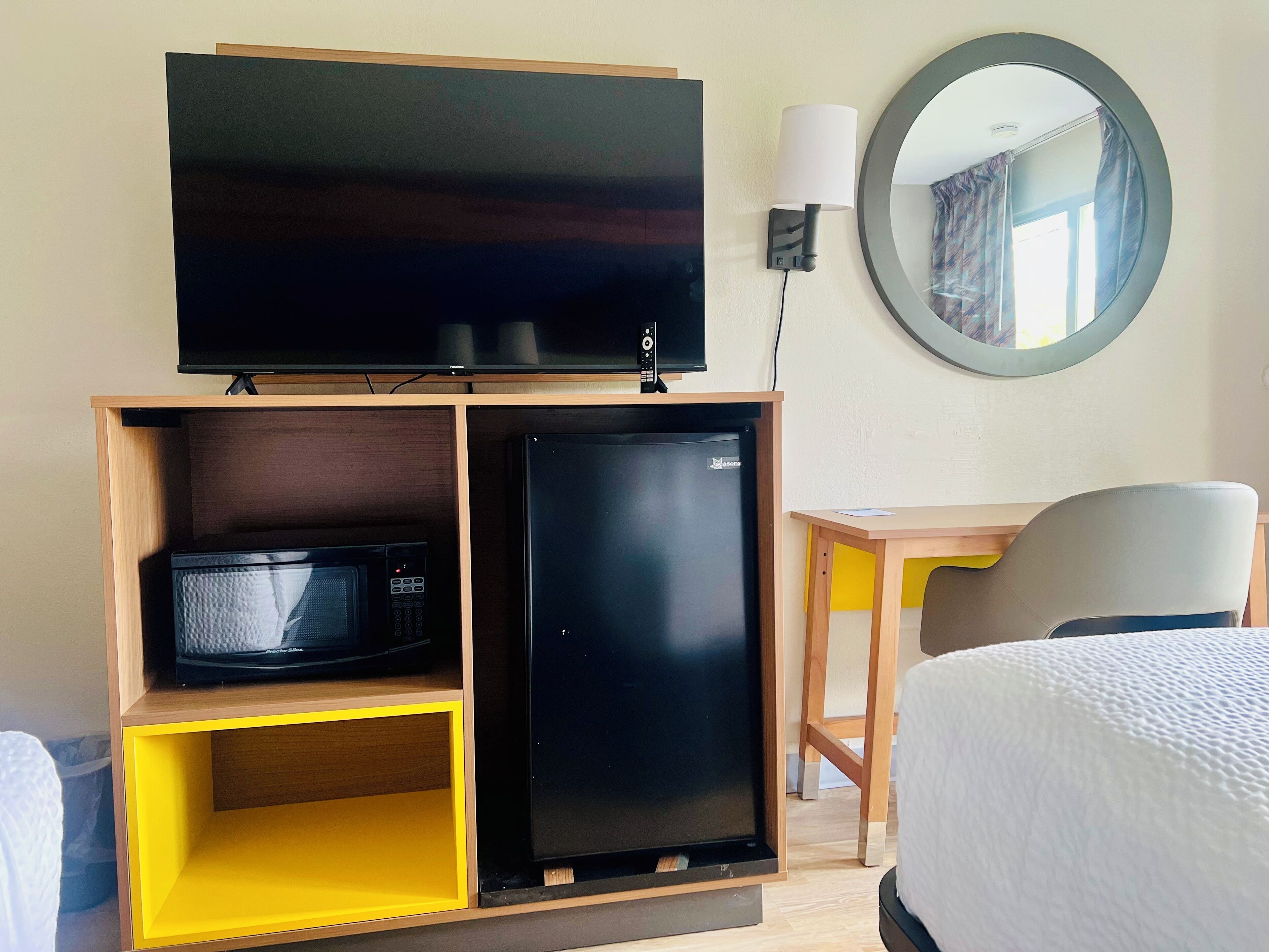 A hotel room with a television, a microwave, a refrigerator, a desk, a chair, and a bed.