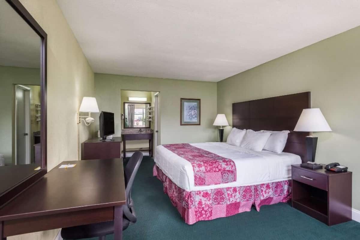 Ein Hotelzimmer mit einem Bett, zwei Nachttischen, einem Schreibtisch, einem Stuhl, einem Spiegel und einer Tür zu einem Badezimmer.