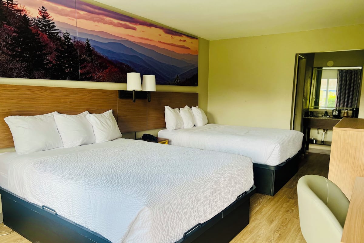 Ein Hotelzimmer mit zwei Betten, einem hölzernen Kopfteil, einem Gemälde von einer Berglandschaft und einem kleinen Schreibtisch mit Stuhl.