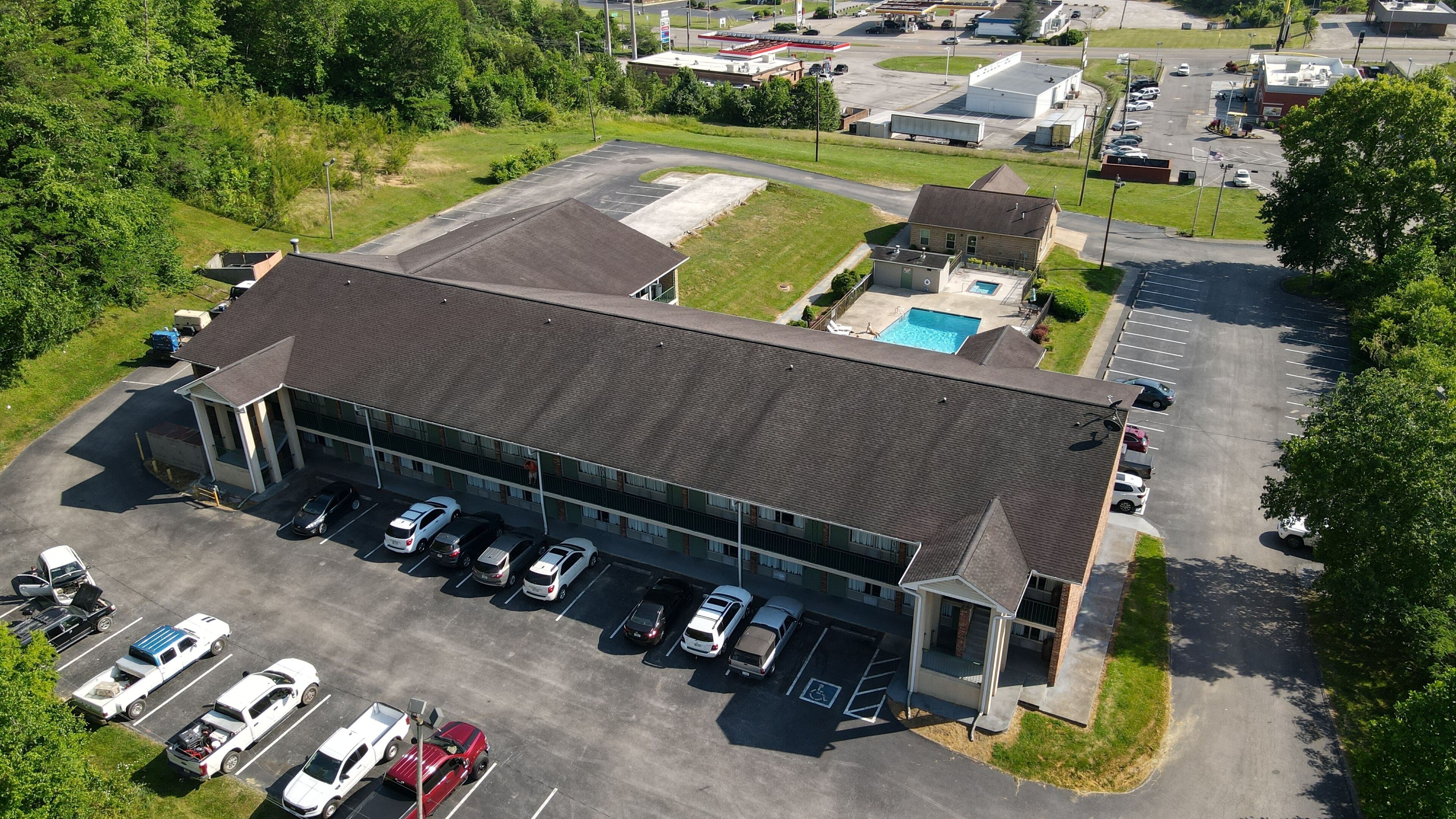 An aerial view of a building with a parking lot, a swimming pool, and a gas station in the background.