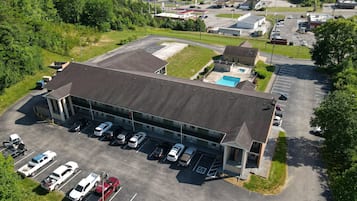 Vista aérea de um edifício com estacionamento, piscina e posto de gasolina ao fundo.