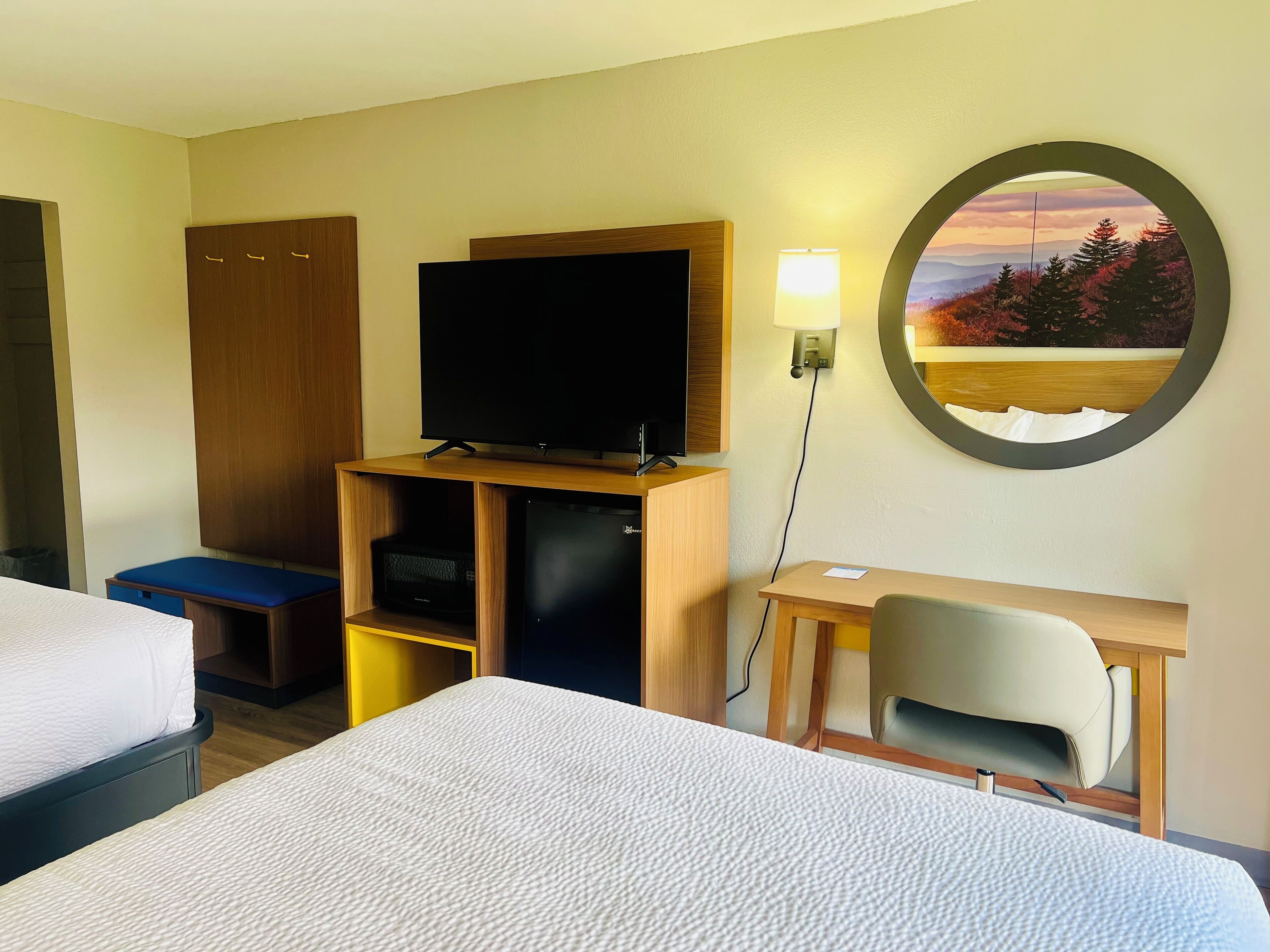 A hotel room with a bed, a desk, a television, a chair, and a wall-mounted mirror.
