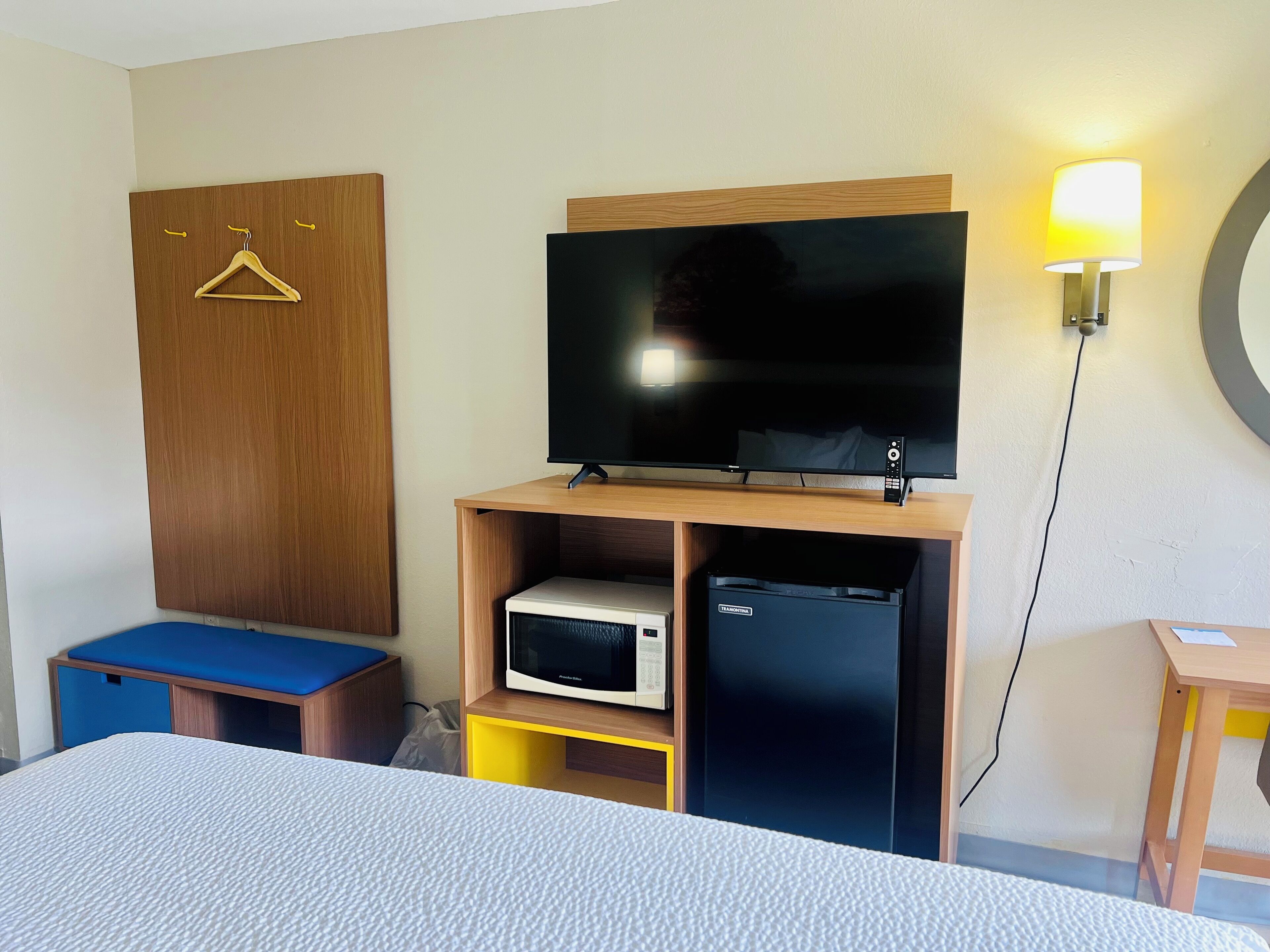 A hotel room with a bed, a television on a wooden stand, a microwave, and a small table.