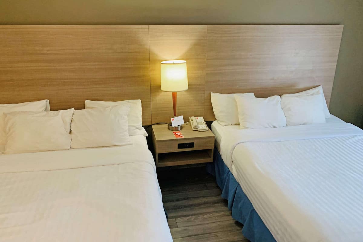 A hotel room with two beds, a nightstand with a lamp, a phone, and a card holder.