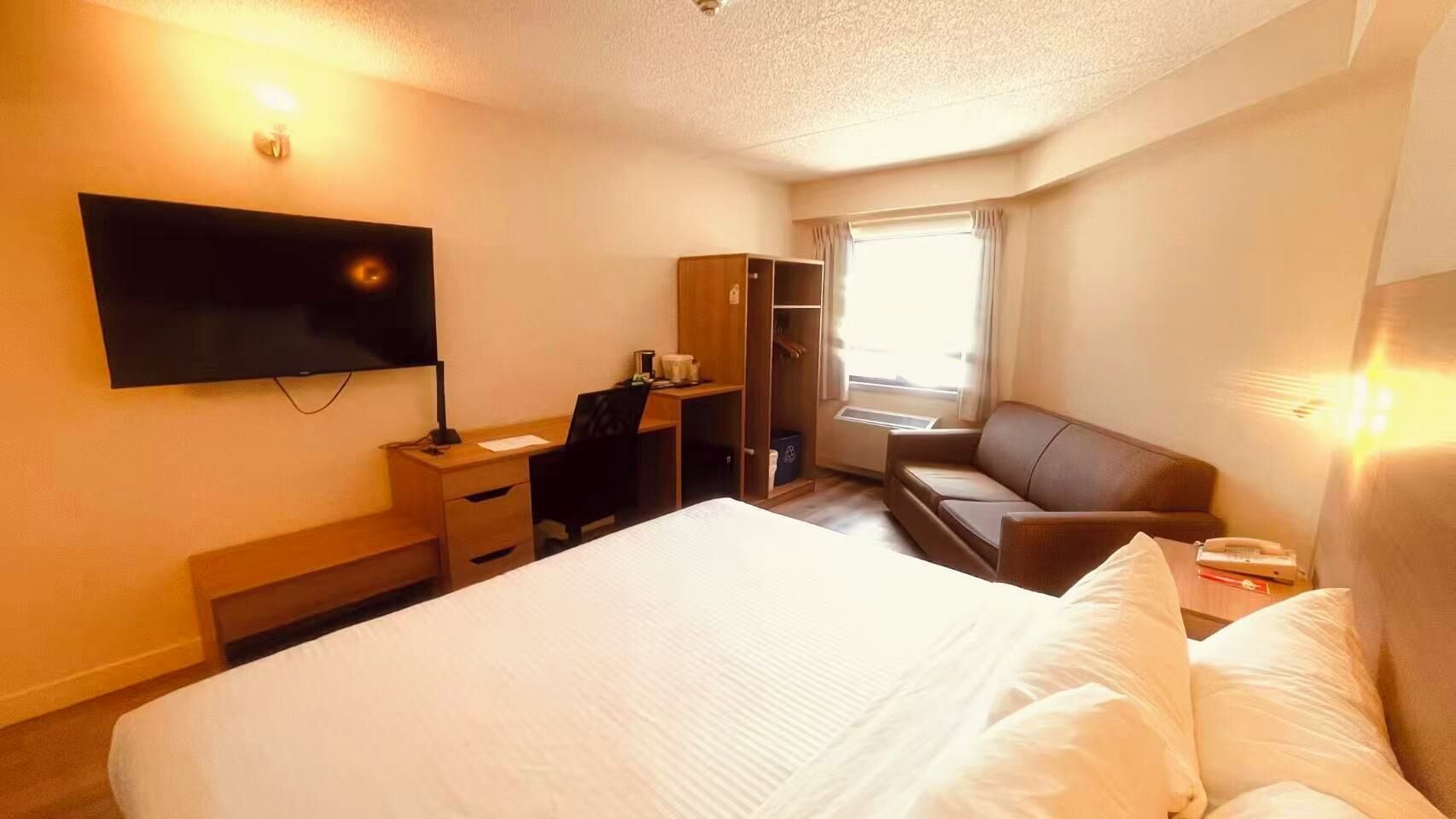 A hotel room with a bed, a desk, a chair, a television, a wardrobe, and a window.