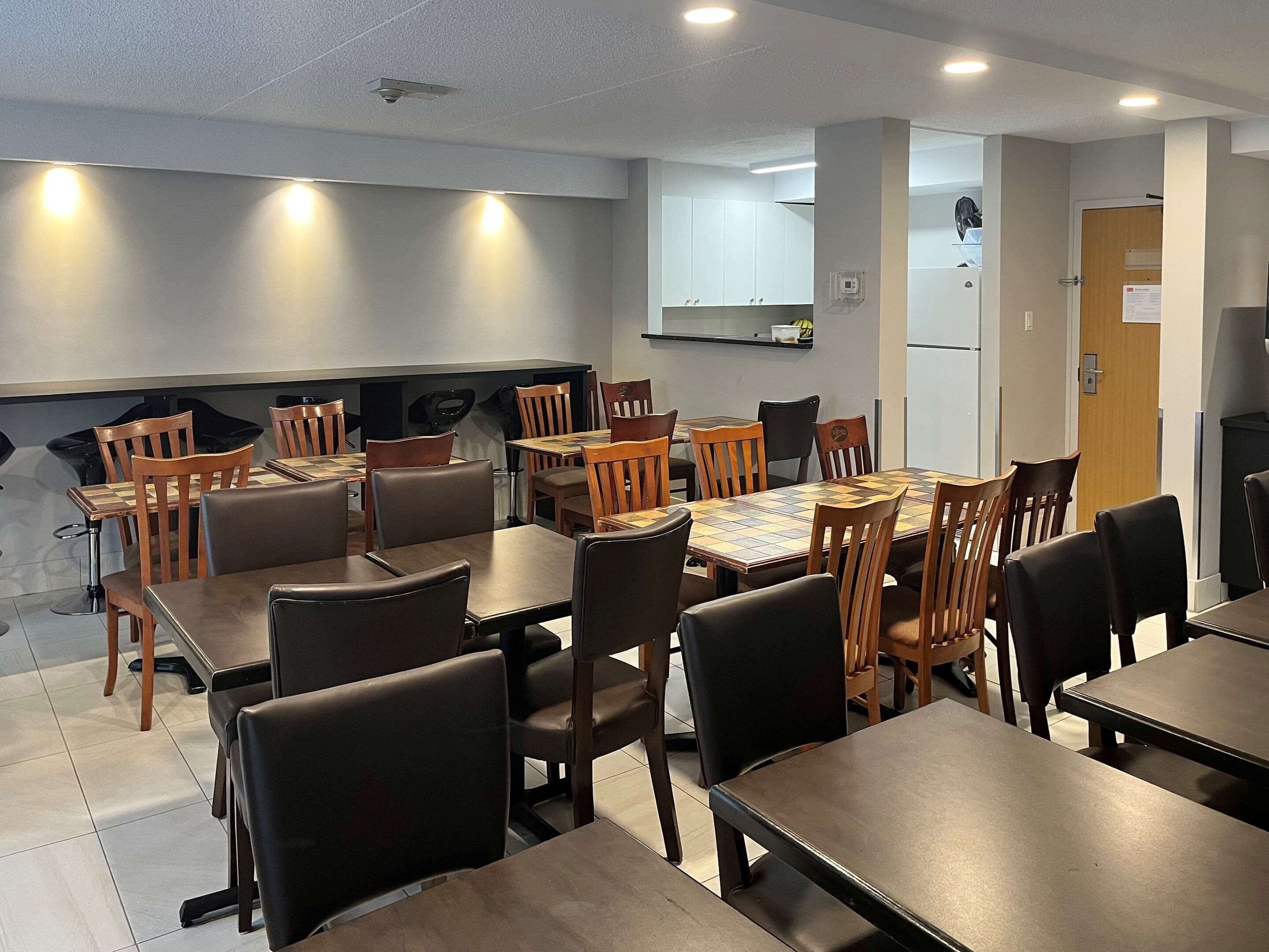 Un comedor con varias mesas y sillas, una zona de cocina con armarios y una puerta que da a otra habitación.