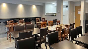 Un comedor con varias mesas y sillas, una zona de cocina con armarios y una puerta que da a otra habitación.