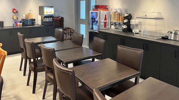 Un café moderno con mesas y sillas de madera oscura, una máquina de café, un refrigerador y un mostrador de comida.