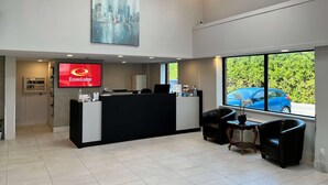 Un moderno vestíbulo de hotel con mostrador de recepción, un cuadro grande y vista a un coche azul en el exterior.