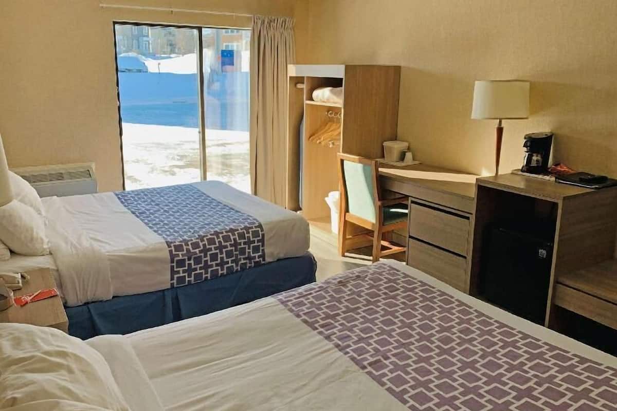 A hotel room with two beds, a desk, a chair, a wardrobe, and a view of the outdoors.