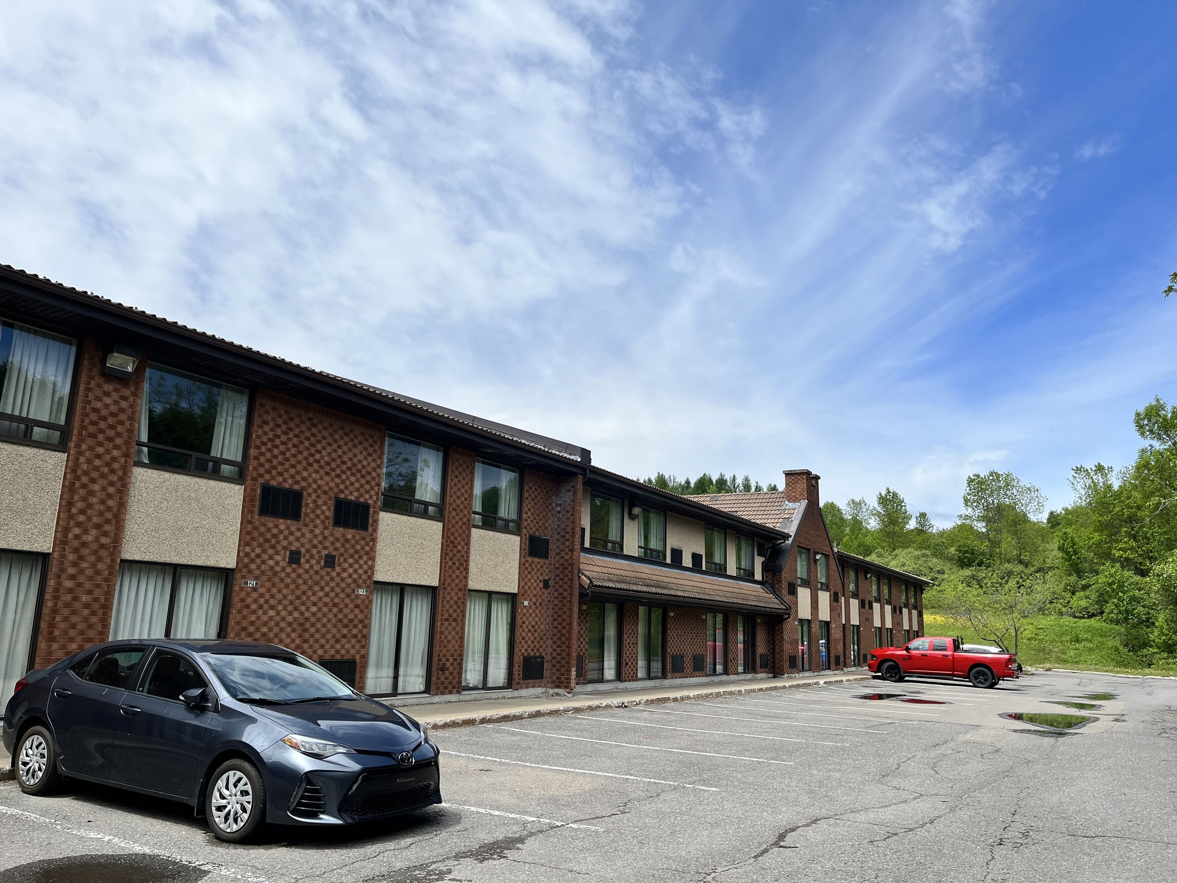Un edificio de varios pisos con fachada de ladrillo, ventanas amplias y un estacionamiento con automóviles.