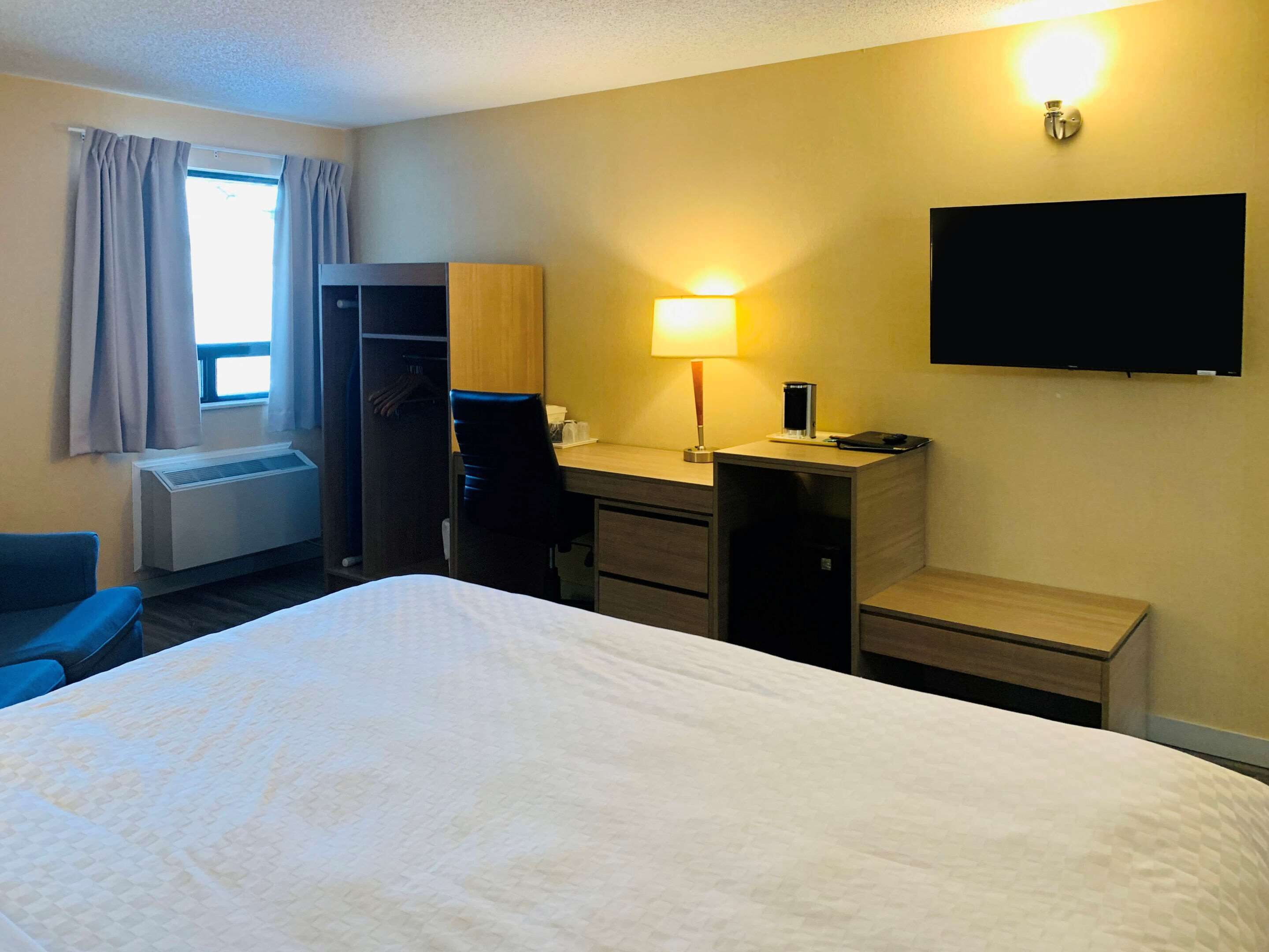 A hotel room with a bed, a desk, a chair, a TV, and a window with curtains.