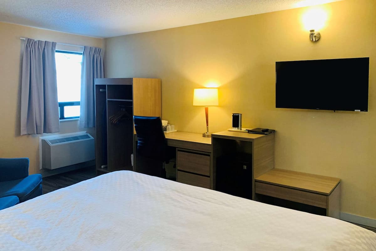 A hotel room with a bed, a desk, a chair, a TV, and a window with curtains.