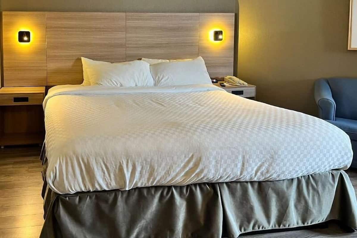 A hotel room with a large bed, two bedside lamps, a nightstand, and a chair.