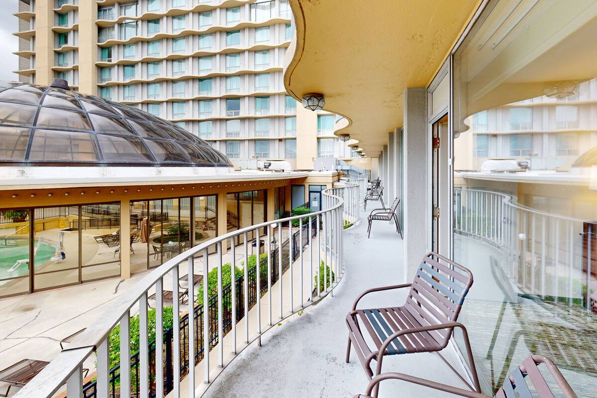 A balcony with a glass balustrade, a pool, and a view of a high-rise building.