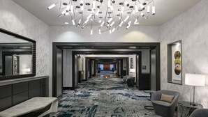 Un hall d’hôtel avec un long couloir, un banc, une chaise, une lampe et un luminaire au plafond.