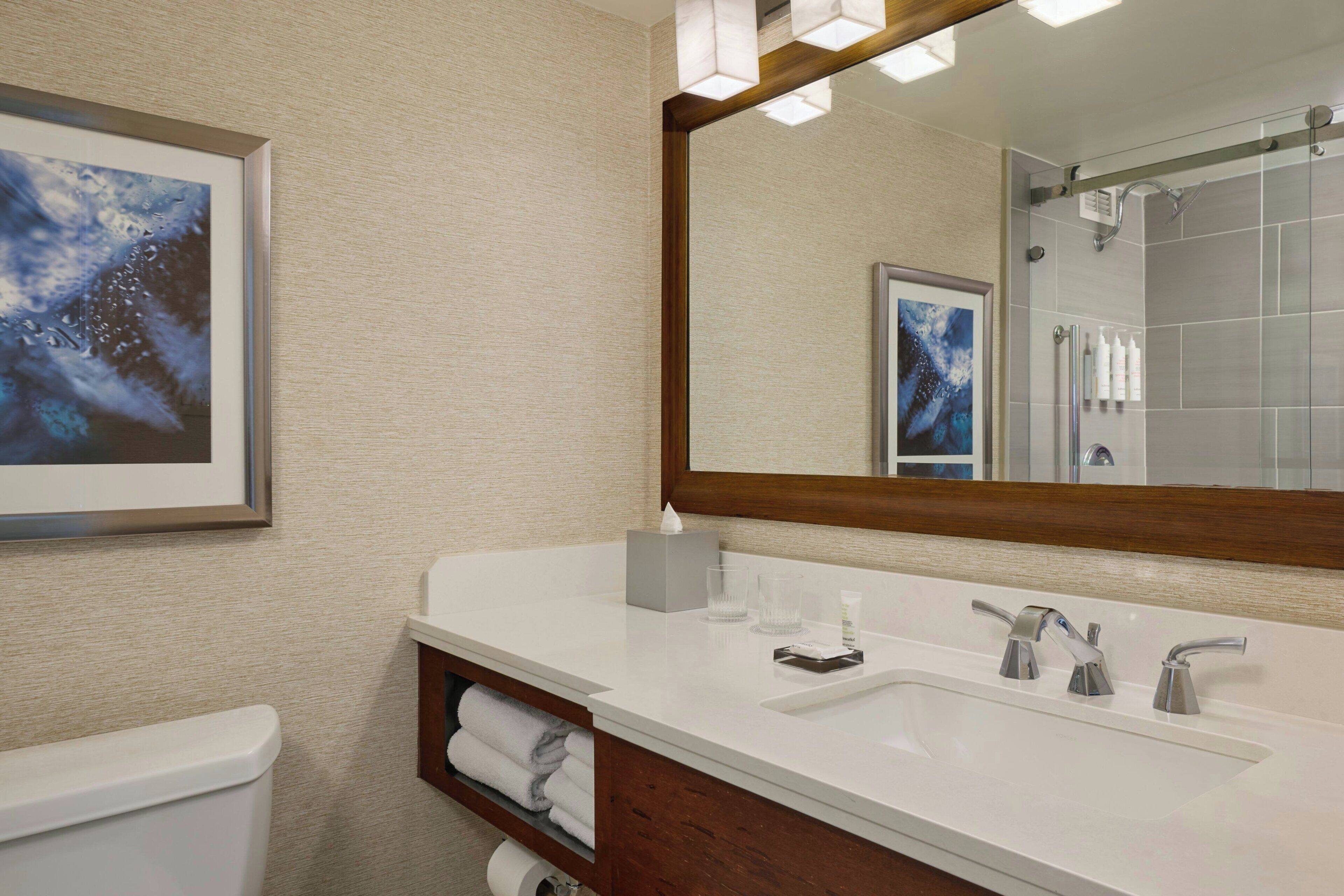 A hotel bathroom with a large mirror, a white sink, a toilet, and a towel rack.