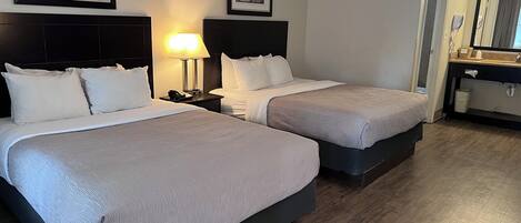 Een hotelkamer met twee bedden, een nachtkastje met lamp, een spiegel, en een badkamer met wastafel en toilet.