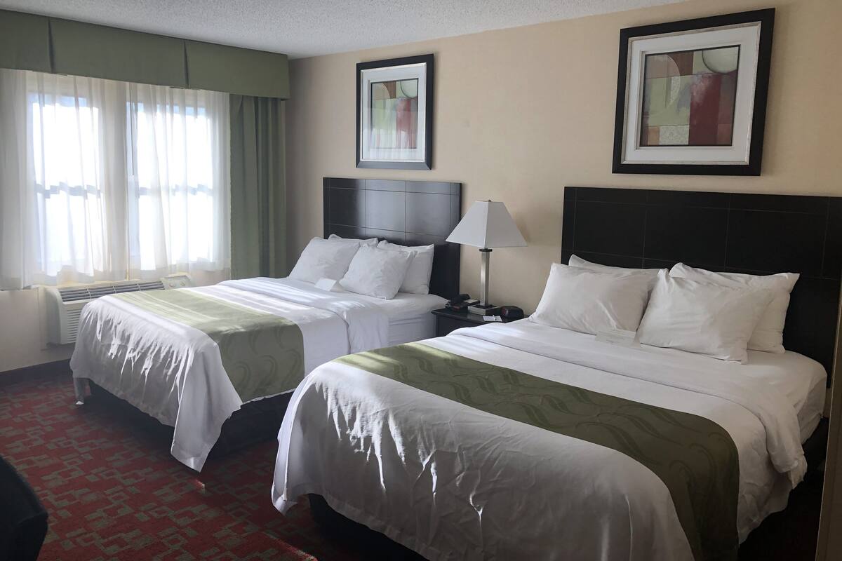 Ein Hotelzimmer mit zwei Betten, einem Schreibtisch und einem Sessel. An der Wand hängen zwei gerahmte Bilder.