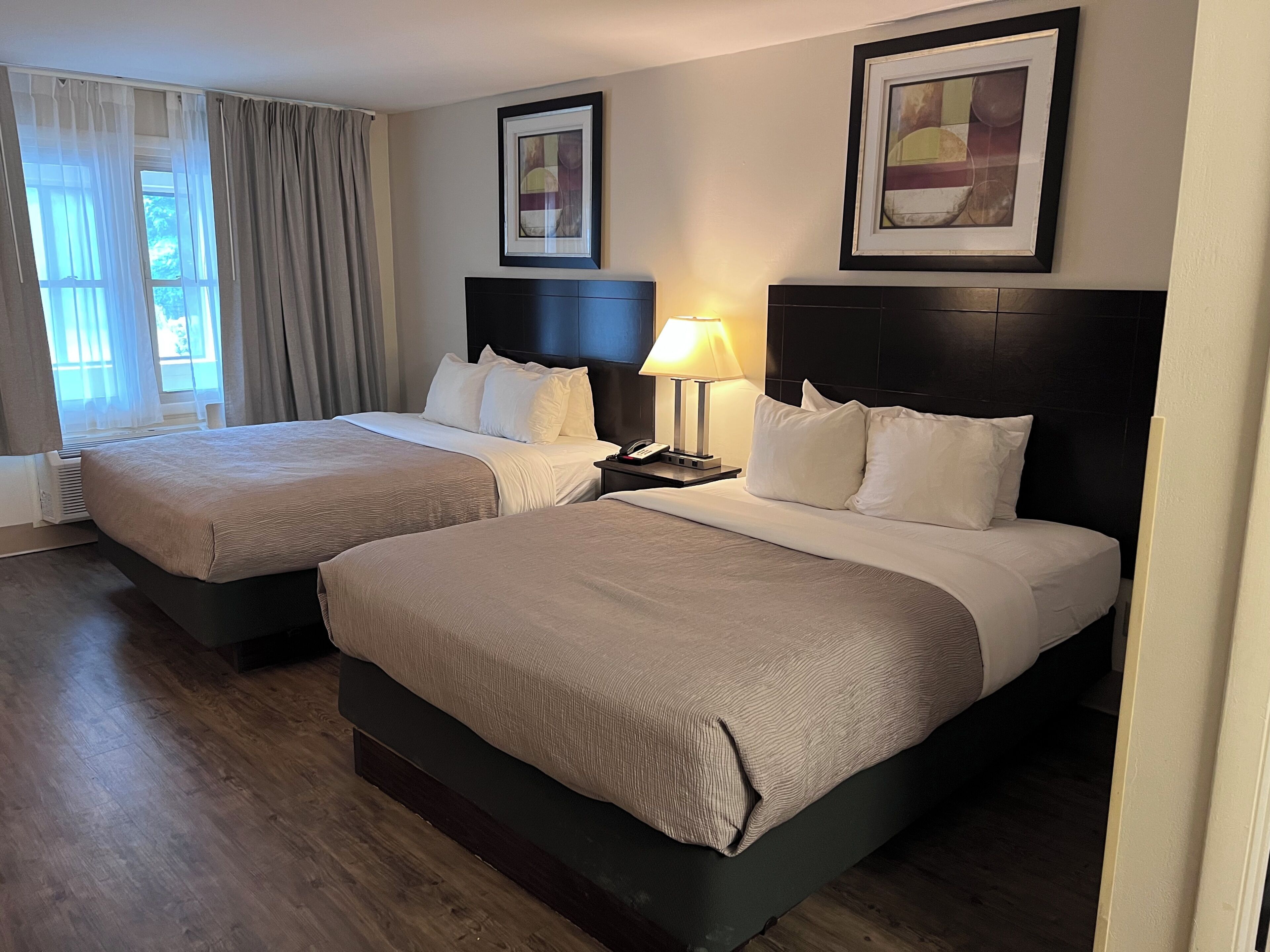 A hotel room with two beds, a bedside lamp, a telephone, and a window with curtains.