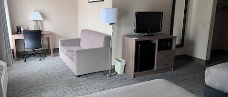 Habitación de hotel con sofá, escritorio, televisor, microondas y un basurero.