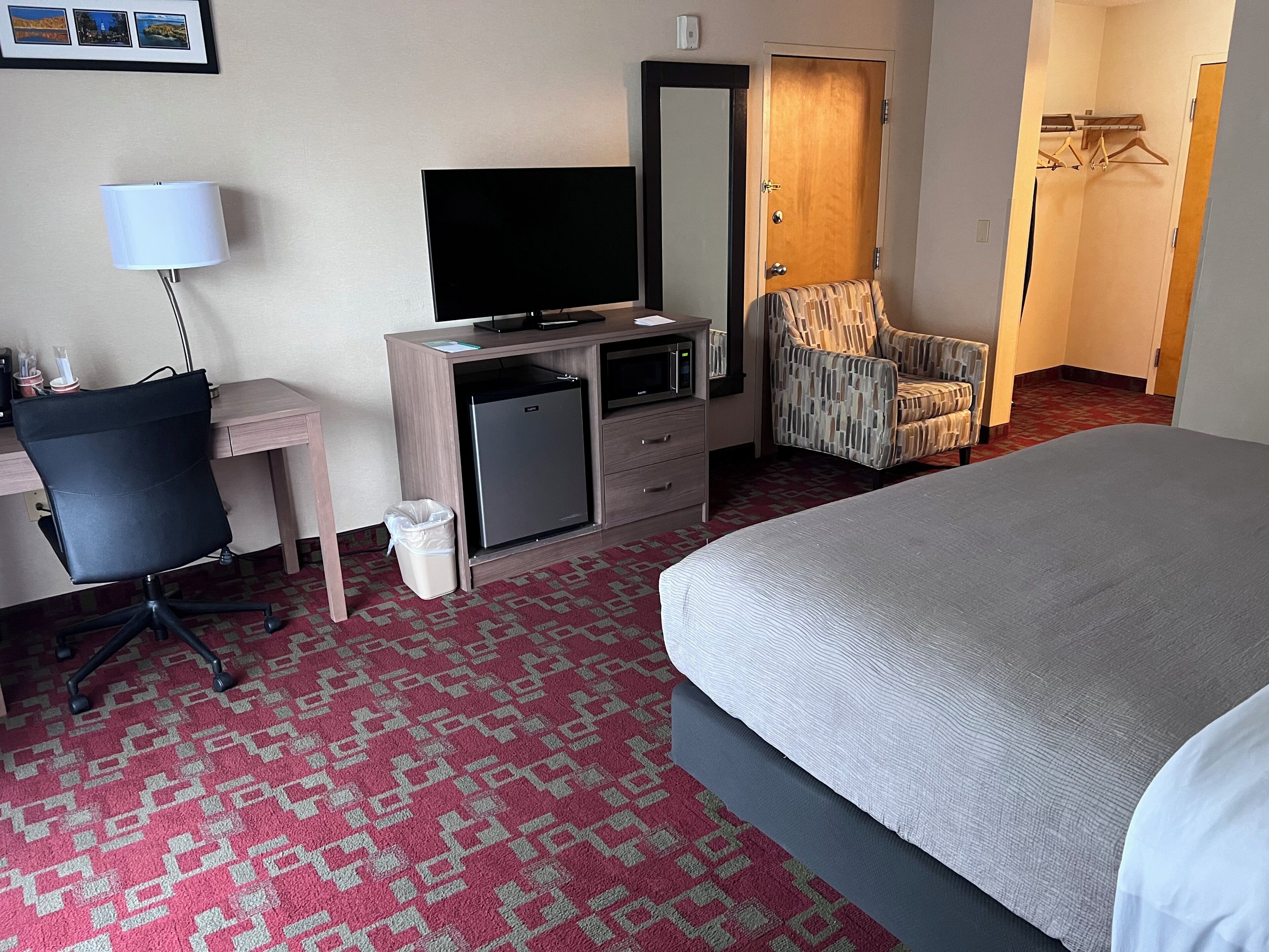 Une chambre d’hôtel comprenant un lit, un bureau avec un ordinateur, une télévision, un petit réfrigérateur, une chaise et une armoire.